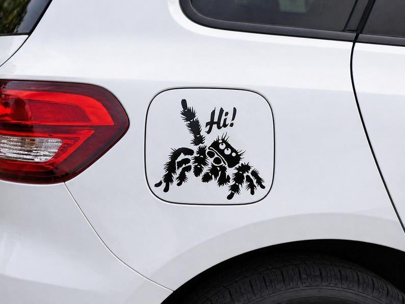 Puede incluir: Una calcoman&iacute;a negra de ara&ntilde;a con la palabra "Hi!" sobre un fondo blanco, adherida a la tapa del combustible de un coche blanco. La ara&ntilde;a tiene un dise&ntilde;o de dibujos animados con ojos grandes y patas peludas. Un divertido accesorio decorativo para el coche.