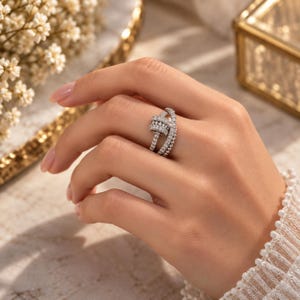 Op de afbeelding: Een zilverkleurige ring met een meerlaags bandontwerp, ingelegd met talloze kleine, heldere, rondgeslepen stenen. De band bestaat uit verschillende in elkaar verstrengelde strengen die een textuurrijk en sprankelend uiterlijk op de vinger creëren.