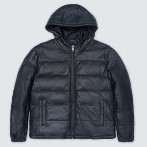 Könnte beinhalten: Marineblaue Leder-Steppjacke mit Kapuze. Die Jacke hat einen durchgehenden Reißverschluss und zwei Seitentaschen. Das Steppmuster sorgt für Textur und Wärme. Ein stilvolles Oberbekleidungsstück für kaltes Wetter.