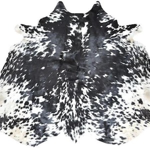 May include: A cowhide rug with a natural pattern of black spots on a white background. The rug has an irregular shape, with a textured surface and a soft appearance. The rug is suitable for home decor.