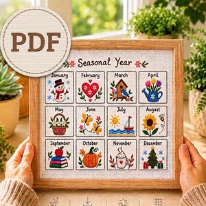 Puede incluir: Un patrón de punto de cruz enmarcado titulado Seasonal Year que presenta doce cuadrados, cada uno representando un mes con iconos bordados como un muñeco de nieve, corazón, pajarera, flores, mariposa, velero, girasol, libros, calabaza, cacao y árbol.