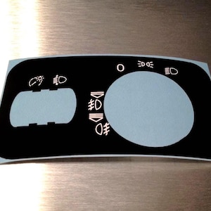 Könnte beinhalten: Schwarze und hellblaue Armaturenbrett-Overlay mit weißen Symbolen für Lichter und Bedienelemente. Das Overlay hat einen großen kreisförmigen Bereich und einen rechteckigen Bereich mit verschiedenen Symbolen.