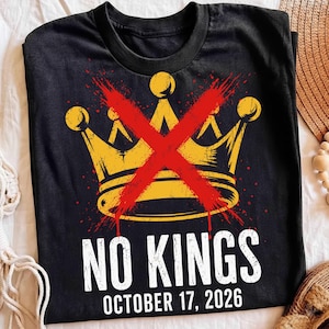 May include: A black short-sleeve t-shirt featuring a yellow graphic of a crown with a large red X mark across it. Below the crown, the text reads NO KINGS in white capital letters, followed by the date OCTOBER 17, 2026 in smaller white text.