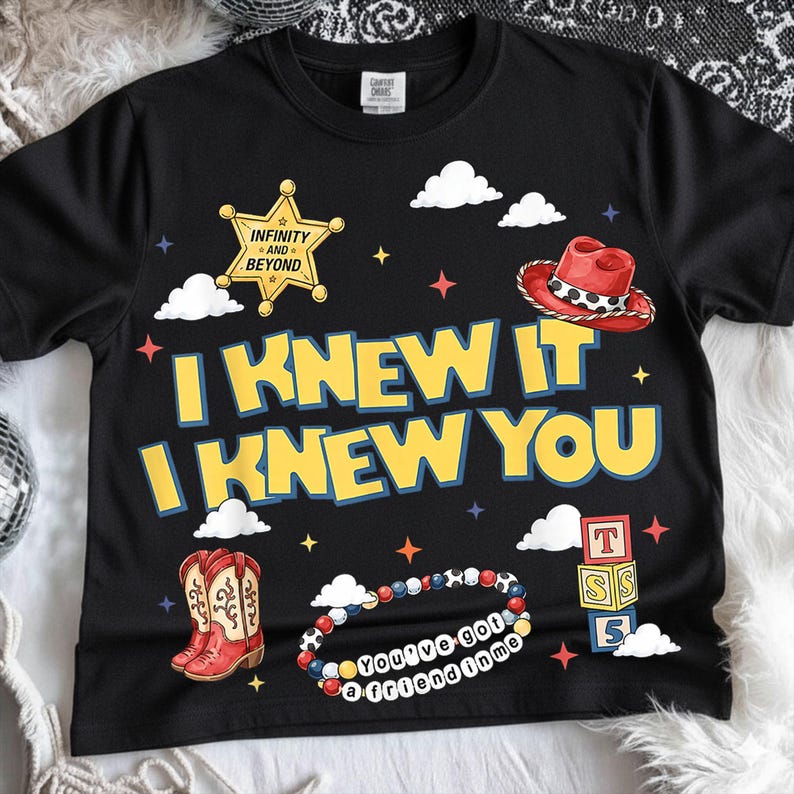 May include: A black t-shirt featuring the yellow text I KNEW IT I KNEW YOU, a yellow sheriff star with the text INFINITY AND BEYOND, a red cowboy hat, red cowboy boots, a stack of three colorful alphabet blocks, and a beaded bracelet with the text YOU'VE GOT A FRIEND IN ME.