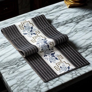 Peut inclure: Chemin de table décoratif avec un motif floral central blanc et bleu, encadré par une bordure géométrique. Les côtés du chemin de table présentent des rayures verticales noires et blanches, créant un motif contrasté. Ce chemin de table élégant est conçu pour la décoration intérieure.