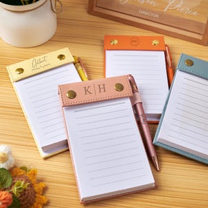 Peut inclure: Quatre blocs-notes rectangulaires avec des couvertures en similicuir jaune, orange, rose et bleu. Chaque bloc comporte un rabat supérieur fixé par deux rivets métalliques dorés, du papier ligné blanc et un stylo assorti gravé d'un nom.