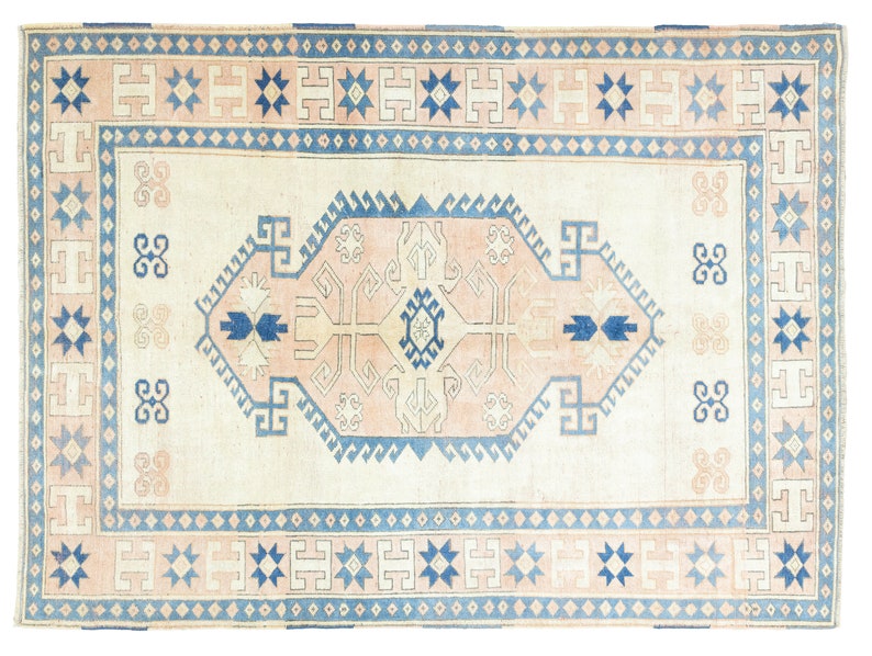 May include: A vintage rug with a cream background and a blue and pink geometric pattern. The rug has a border with a repeating star design.