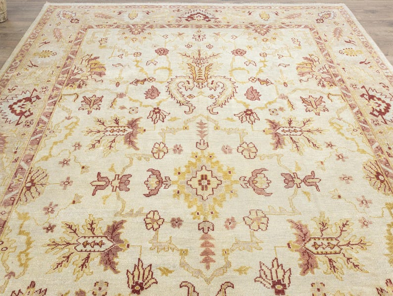 May include: A cream-colored rug with a traditional Persian design. The rug features intricate floral patterns in shades of red, brown, and gold.