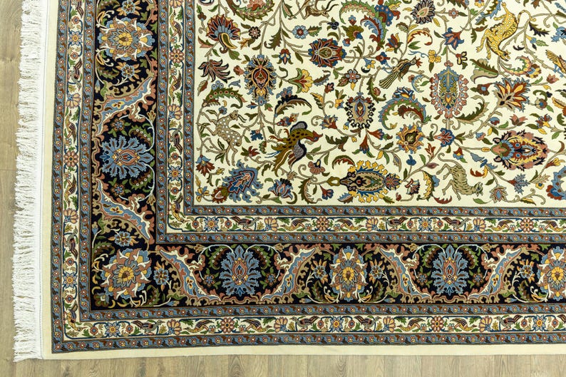 May include: Close-up of an ornate, cream-colored rug with a detailed floral pattern. The rug features a black border with blue and gold floral designs, and a cream fringe along one edge. The central design includes various flowers and animal figures.