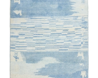 May include: A blue and white patterned rug with a geometric design. The rug has a faded, vintage look and is made of a soft, woven material.
