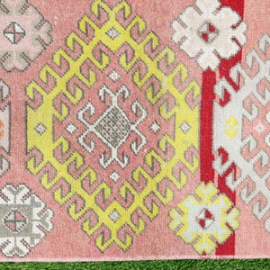 May include: A pink, yellow, white, and red patterned rug with a geometric design. The rug has a fringe border.