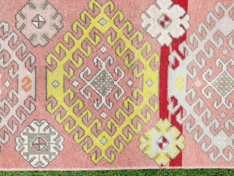 May include: A pink, yellow, white, and red patterned rug with a geometric design. The rug has a fringe border.
