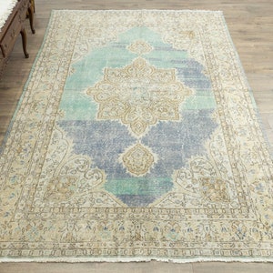 May include: A large, rectangular area rug with a distressed, vintage appearance. The rug features a central medallion design in beige and light blue, surrounded by a border in similar tones. The rug's color palette includes shades of blue, beige, and cream.