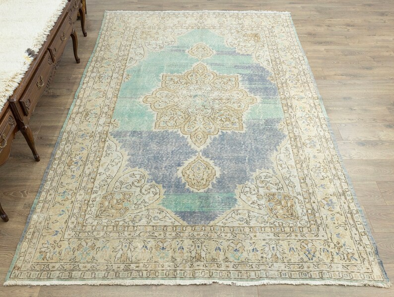 May include: A large, rectangular area rug with a distressed, vintage appearance. The rug features a central medallion design in beige and light blue, surrounded by a border in similar tones. The rug's color palette includes shades of blue, beige, and cream.