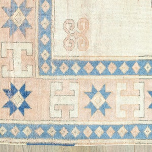 May include: Close-up of a beige rug with a blue and white geometric pattern. The rug has a fringed border and features a repeating star design.