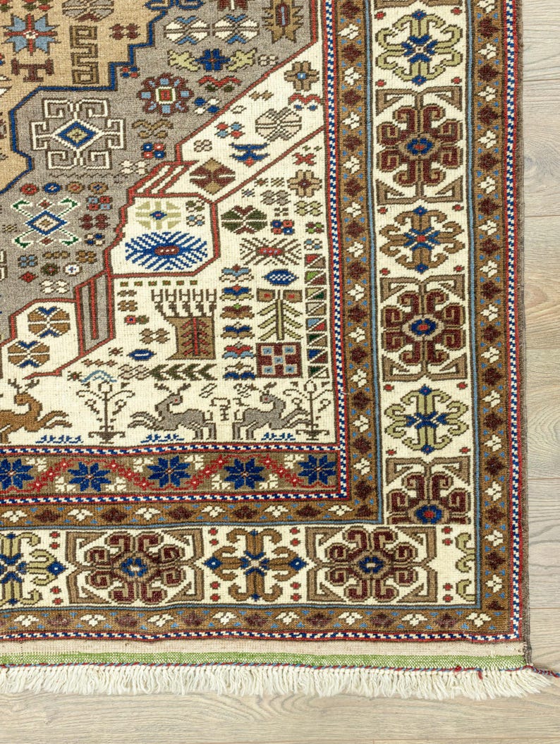 May include: Close-up of a cream-colored rug with a detailed geometric pattern in shades of brown, red, blue, and green. The rug has a fringe border.
