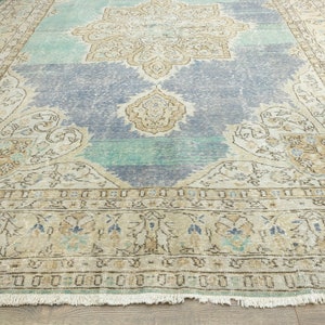 May include: A large, rectangular area rug with a distressed, vintage appearance. The rug features a central medallion design in beige and blue, with a light blue and green background. The border is a lighter beige with a fringe.