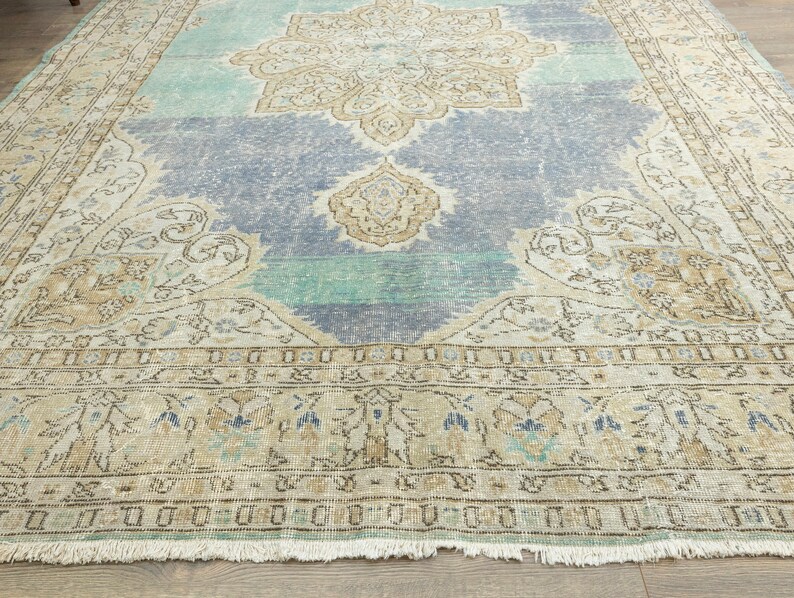 May include: A large, rectangular area rug with a distressed, vintage appearance. The rug features a central medallion design in beige and blue, with a light blue and green background. The border is a lighter beige with a fringe.
