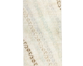 May include: Rectangular off-white rug with a geometric pattern. The rug features a repeating square design with diagonal brown stepped accents. The rug is a neutral color, suitable for various interior design styles.