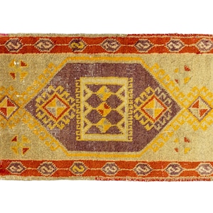 May include: A vintage rug with a geometric pattern in shades of red, orange, yellow, and brown. The rug has a fringed edge and a central medallion.