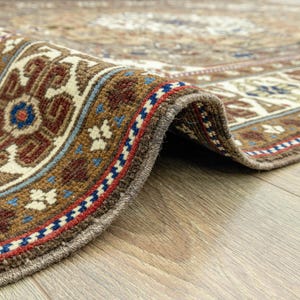 May include: Close-up of the edge of a brown and cream patterned rug with a detailed border of red, blue, and white. The rug is folded over and the edge is visible.