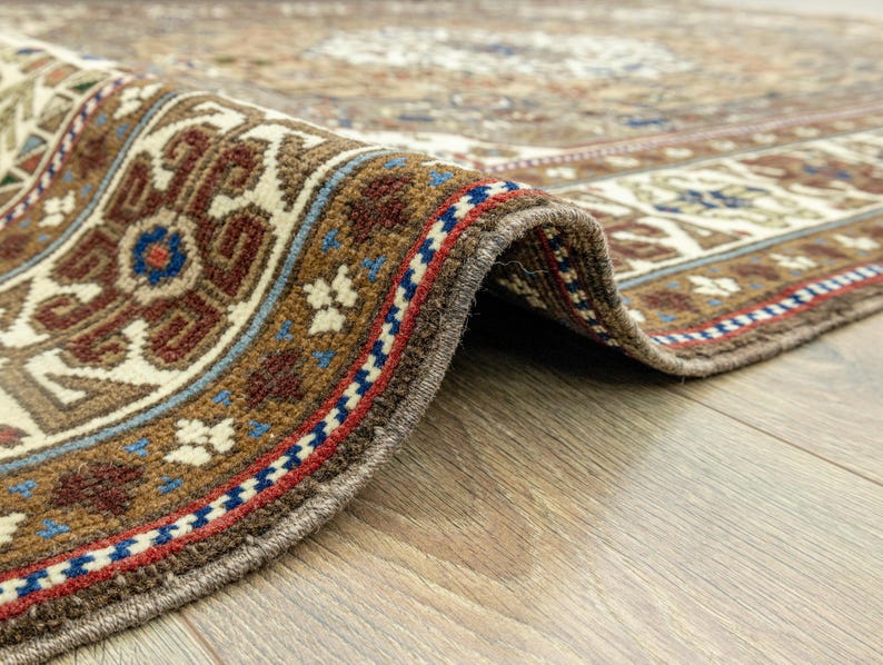 May include: Close-up of the edge of a brown and cream patterned rug with a detailed border of red, blue, and white. The rug is folded over and the edge is visible.
