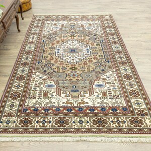 May include: A traditional cream-colored rug with a detailed floral and geometric pattern in shades of brown, red, and blue. The rug has a fringe border.