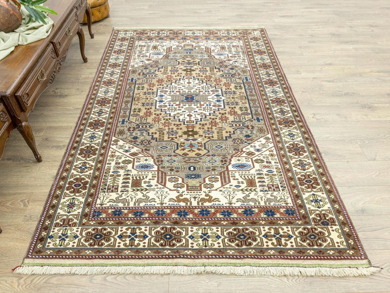 May include: A traditional cream-colored rug with a detailed floral and geometric pattern in shades of brown, red, and blue. The rug has a fringe border.