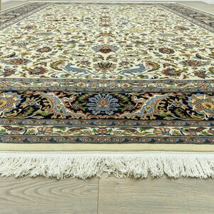 May include: An ivory-colored, rectangular area rug with an intricate floral and bird pattern. The rug features a dark blue border with floral medallions and a cream-colored fringe along the edge. The design includes shades of blue, green, and gold.