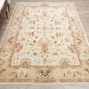 May include: A beige area rug with a detailed floral pattern in shades of red, brown, and yellow. The rug has a cream-colored background and a border with a repeating pattern.