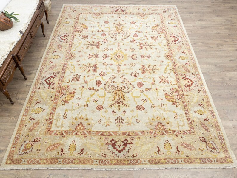 May include: A beige area rug with a detailed floral pattern in shades of red, brown, and yellow. The rug has a cream-colored background and a border with a repeating pattern.