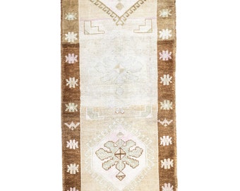 May include: A long, narrow rug with a beige background and brown and pink geometric patterns. The rug has a traditional design with floral motifs and intricate details.