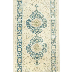 Puede incluir: Una alfombra vintage con fondo crema y un patrón floral azul y verde. La alfombra tiene un borde con un diseño floral repetitivo.