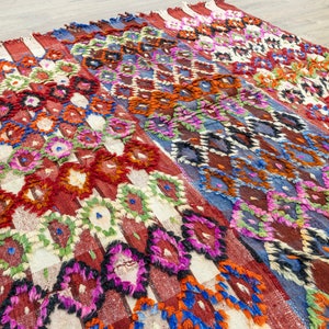 May include: A colorful Moroccan rug with a geometric pattern in shades of red, blue, green, and white. The rug is woven with a thick, textured pile.