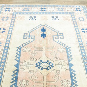 May include: A vintage rug with a light pink and blue geometric pattern. The rug has a cream background and features a central medallion with a starburst design.
