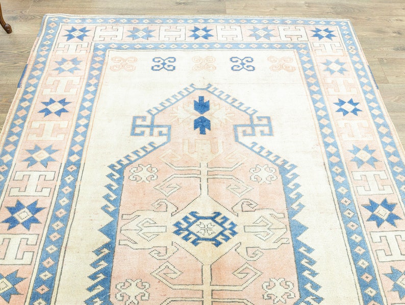 May include: A vintage rug with a light pink and blue geometric pattern. The rug has a cream background and features a central medallion with a starburst design.