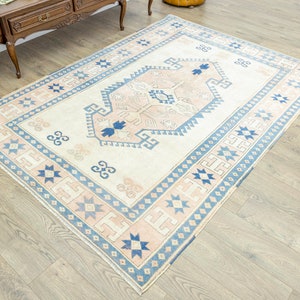 May include: A cream-coloured rug with a blue and pink geometric pattern. The rug has a central medallion with a stylised floral design.