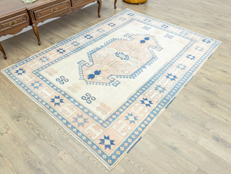 May include: A cream-coloured rug with a blue and pink geometric pattern. The rug has a central medallion with a stylised floral design.