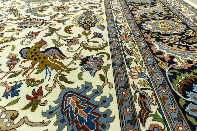 May include: Close-up of a detailed Persian rug with a cream-colored background. The rug features intricate floral and bird patterns in shades of blue, green, brown, and red. The border has a blue and cream floral design.