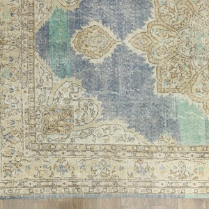 May include: A distressed, vintage-style rug with a faded blue central field and a large, ornate beige medallion. The rug features a detailed border with floral and geometric patterns in beige, blue, and teal. The rug's design suggests a traditional, antique aesthetic.