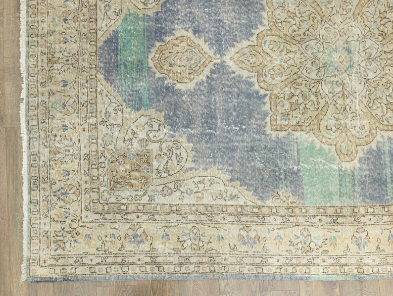 May include: A distressed, vintage-style rug with a faded blue central field and a large, ornate beige medallion. The rug features a detailed border with floral and geometric patterns in beige, blue, and teal. The rug's design suggests a traditional, antique aesthetic.