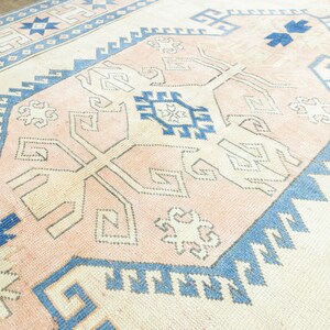 May include: A vintage rug with a light pink background and a geometric pattern in shades of blue and white.