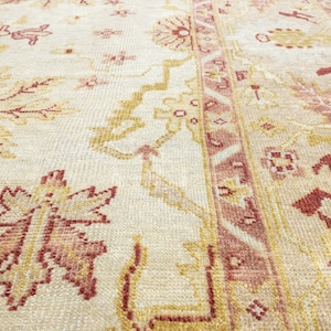 May include: A close-up of a cream-colored rug with a pink and yellow floral pattern. The rug has a detailed design with intricate details.