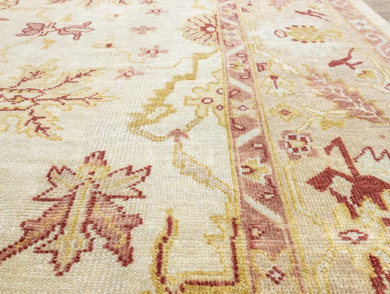 May include: A close-up of a cream-colored rug with a pink and yellow floral pattern. The rug has a detailed design with intricate details.