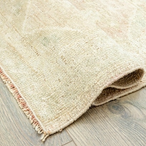 May include: A cream-colored rug with a fringed edge. The rug is folded in half and has a subtle pattern.