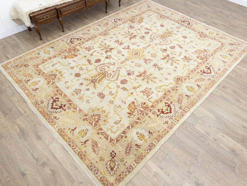 Oversized vintage Turkish Oushak rug with a creamy ivory field, muted blush and golden ochre botanical motifs, and wide traditional floral borders.