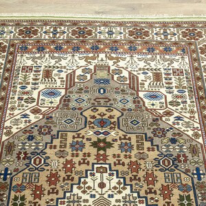 May include: A traditional rug with a cream background and intricate geometric patterns in shades of brown, red, blue, and green. The rug features a central medallion with a repeating pattern of stylized flowers and leaves.