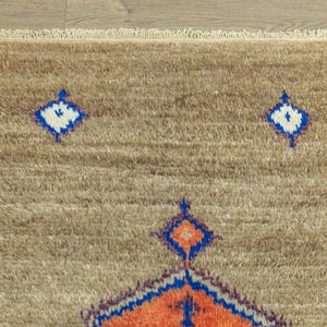 Peut inclure: Gros plan sur un tapis beige avec une surface textur&eacute;e et une bordure &agrave; franges. Le tapis pr&eacute;sente un motif r&eacute;p&eacute;titif de losanges bleus, blancs et oranges. Le tapis est fait d'une mati&egrave;re douce et moelleuse.