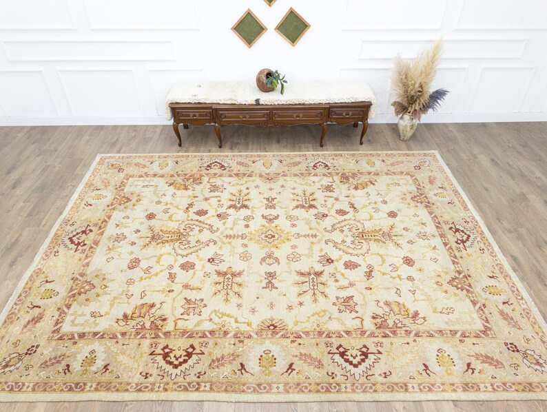 May include: A cream-colored rug with a detailed floral pattern in shades of red and beige. The rug has a border with a repeating geometric design.