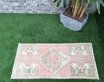 May include: A pink and cream patterned runner rug with fringed edges. The rug is laid out on a green artificial grass surface.